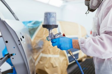 Koruyucu giysi ve sprey kompresör kullanarak maske resim araba olan adam. Seçici odak.