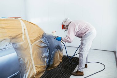 Koruyucu giysi ve sprey kompresör kullanarak maske resim araba olan adam. Seçici odak.