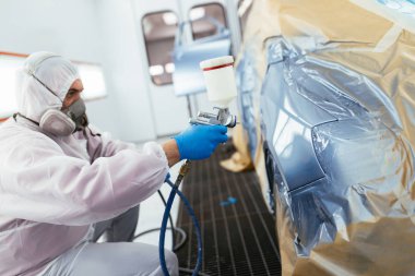 Koruyucu giysi ve sprey kompresör kullanarak maske resim araba olan adam. Seçici odak.