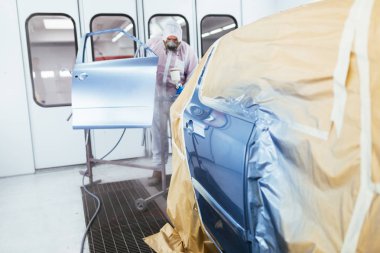 Koruyucu giysi ve sprey kompresör kullanarak maske resim araba olan adam. Seçici odak.