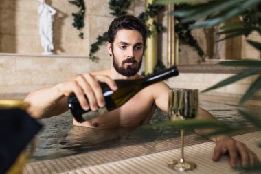 Zevk ve spa merkezinde rahatlatıcı yakışıklı delikanlı. Jakuzide oturma ve şarap içme.