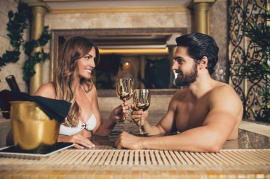 Zevk ve Spa merkezinde rahatlatıcı güzel genç bir çift. Hidro masaj havuzu oturuşta ve şarap içme