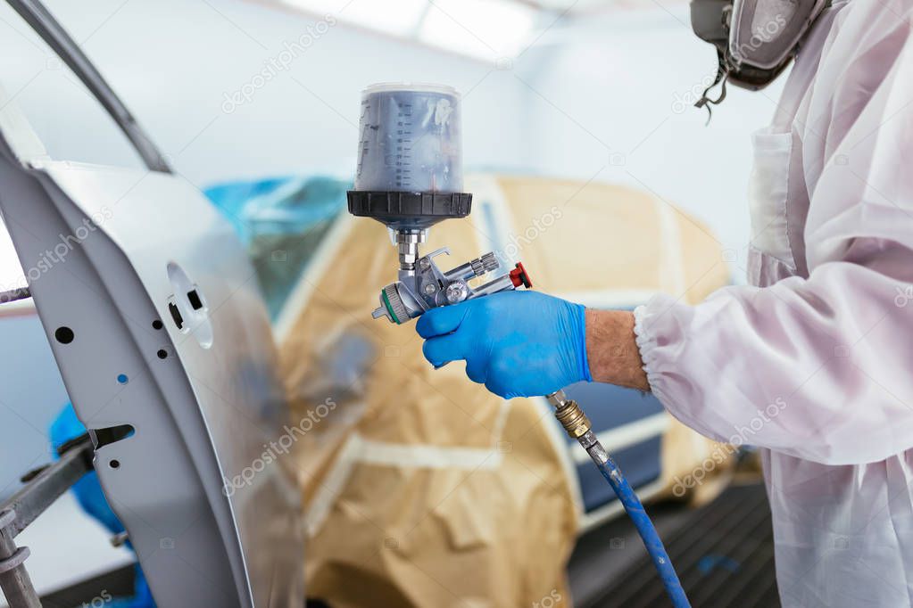 Man with protective clothes and mask painting car using spray compressor. Selective focus.