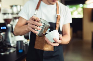 Taze kahve yapma prosedürü. Profesyonel barista kahve bardağına süt dolduruyor..