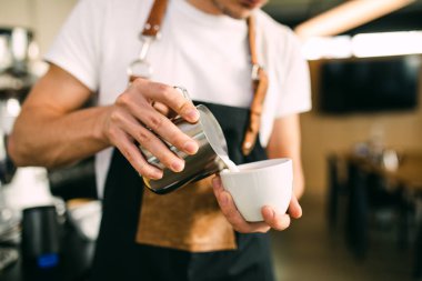 Taze kahve yapma prosedürü. Profesyonel barista kahve bardağına süt dolduruyor..