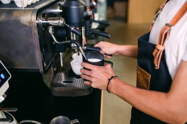 Taze kahve yapma prosedürü. Profesyonel barista kahve bardağına süt dolduruyor..