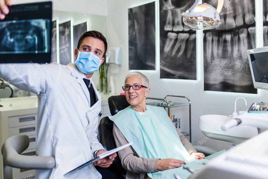 Handsome smiling dentist looking at x-ray image of his senior woman patient.  