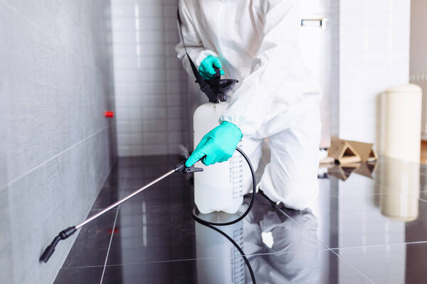 Exterminator in work wear spraying pesticide with sprayer.