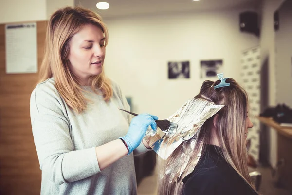 Hairdresser is dying female hair, making hair highlights to his client with a foil.