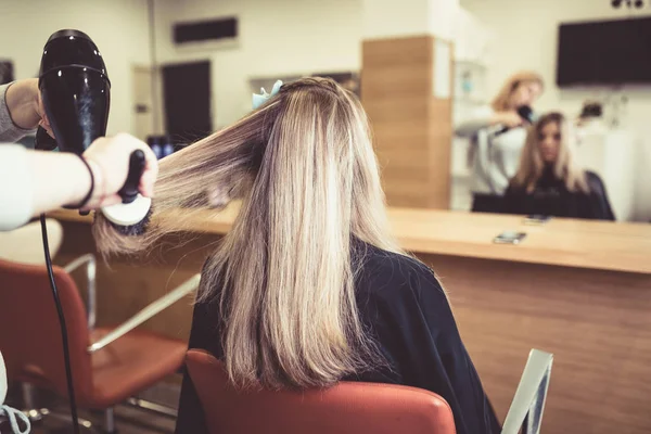 Beautiful hairstyle of young woman after drying hair and making highlights in hair salon.