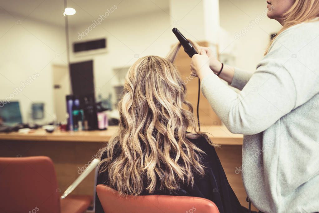 Beautiful hairstyle of young woman after drying hair and making highlights in hair salon. 