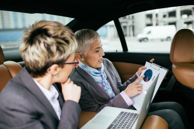 Kıdemli iş kadını ve asistanı limuzin konuşma ve çalışma oturuyor.