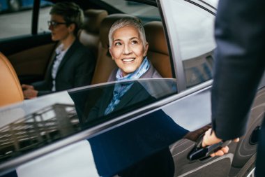 Kıdemli iş kadını ve asistanı limuzin konuşma ve çalışma oturuyor.