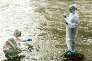 Koruyucu giysili iki bilim adamı nehirden su örnekleri alıyor.