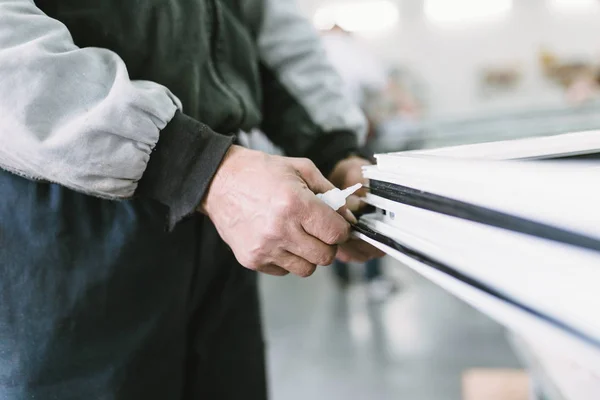 Factory for aluminum and PVC windows and doors production. Manual worker assembling PVC doors and windows. Selective focus.