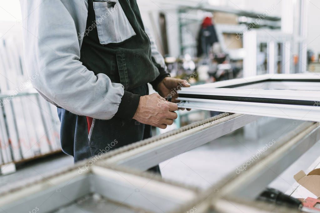 Factory for aluminum and PVC windows and doors production. Manual worker assembling PVC doors and windows. Selective focus. 