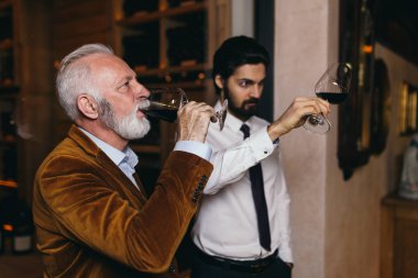 Şarap mahzenindeki şarap üreticileri ellerinde bir kadeh şarap tutup kontrol ediyorlar. Şarap garsonları şaraphanedeki şarapları test ediyor..