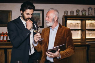 Şarap mahzenindeki şarap üreticileri ellerinde bir kadeh şarap tutup kontrol ediyorlar. Şarap garsonları şaraphanedeki şarapları test ediyor..