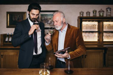 Şarap mahzenindeki şarap üreticileri ellerinde bir kadeh şarap tutup kontrol ediyorlar. Şarap garsonları şaraphanedeki şarapları test ediyor..