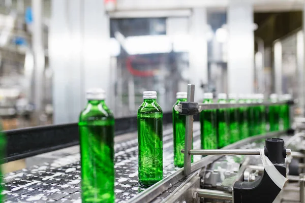 瓶詰めプラント 処理し 緑のガラスボトルに純粋な泉の水を瓶詰めするための水瓶詰めライン 選択フォーカス — ストック写真
