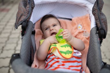 Dışarıda at arabasında yatarken oyuncaklarla oynayan sevimli bir çocuk.