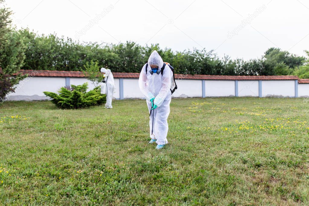 Exterminators outdoors in work wear spraying pesticide with sprayer. 