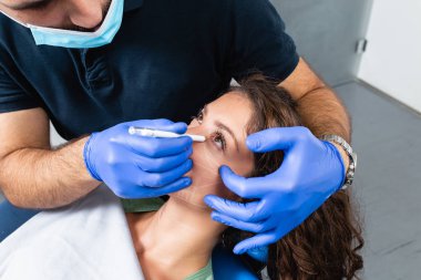 Bir muayene odasında yüzünde düzeltme hatları ile huzurlu genç hasta.