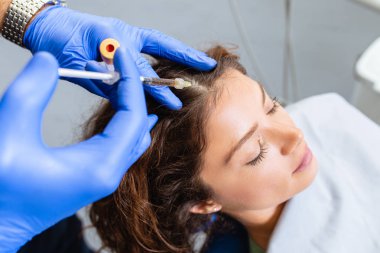 Çekici genç bir kadın canlandırıcı yüz enjeksiyonu yaptırıyor. O, klinikte sakince oturuyor. Uzman güzellik uzmanı hyaluronik asitle kadın kırışıklıklarını dolduruyor..