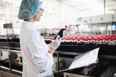 Şişeleme fabrikasındaçalışan kadın işçi sevkiyatöncesi meyve şişelerini kontrol ediyor. Denetim kalite kontrolü.