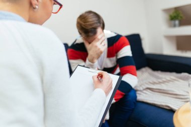 Psikolog ofiste ağlayan hasta ile oturum ve notlar yazma.