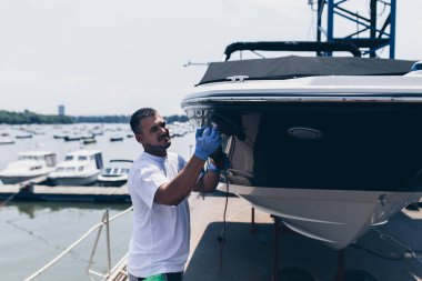 Boat maintenance - Man with orbital polisher polishing boat in marina. Selective focus. clipart
