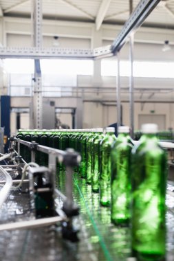 Su fabrikası - saf kaynak suyunu işlemek ve şişelemek için kullanılan su şişeleme hattı küçük yeşil cam şişelere. Seçici odak. 