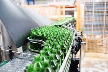 Su fabrikası - saf kaynak suyunu işlemek ve şişelemek için kullanılan su şişeleme hattı küçük yeşil cam şişelere. Seçici odak. 