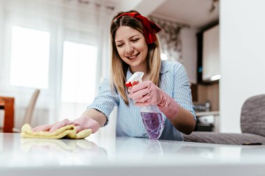 Güzel genç bir kadın mikrofiber bezle evi temizliyor. Oda servisi kavramı.