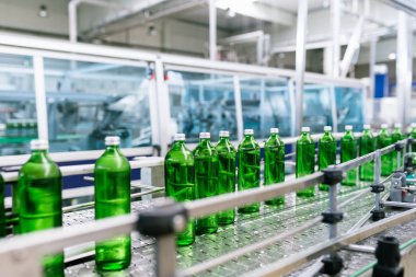 Su fabrikası - saf maden suyunu işlemek ve şişelemek için kullanılan su şişeleme hattı yeşil cam şişelere. Seçici odak.