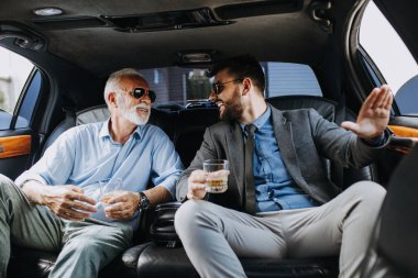 Senior businessman and his assistant sitting in limousine and celebrating their job success. clipart