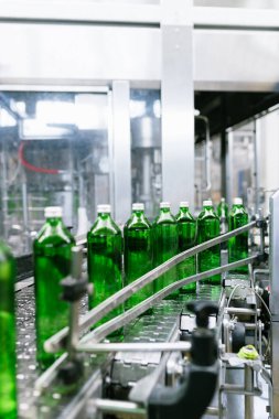 Su fabrikası - saf maden suyunu işlemek ve şişelemek için kullanılan su şişeleme hattı yeşil cam şişelere. Seçici odak.