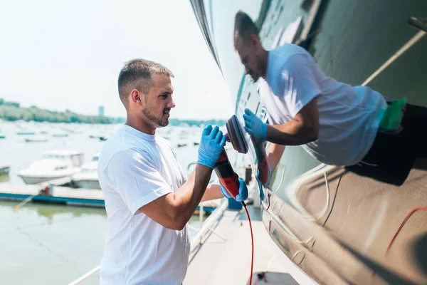 Boat maintenance - Man with orbital polisher polishing boat in marina. Selective focus.