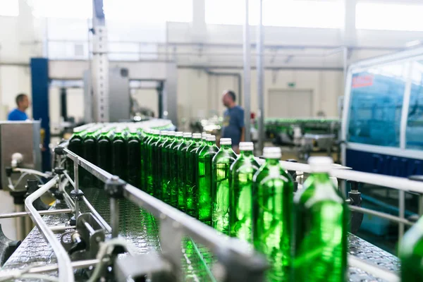 Su fabrikası - saf maden suyunu işlemek ve şişelemek için kullanılan su şişeleme hattı yeşil cam şişelere. Seçici odak.