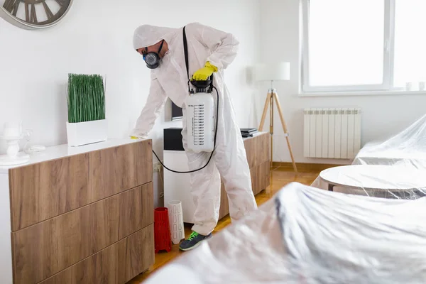 Exterminator in work wear spraying pesticide with sprayer.