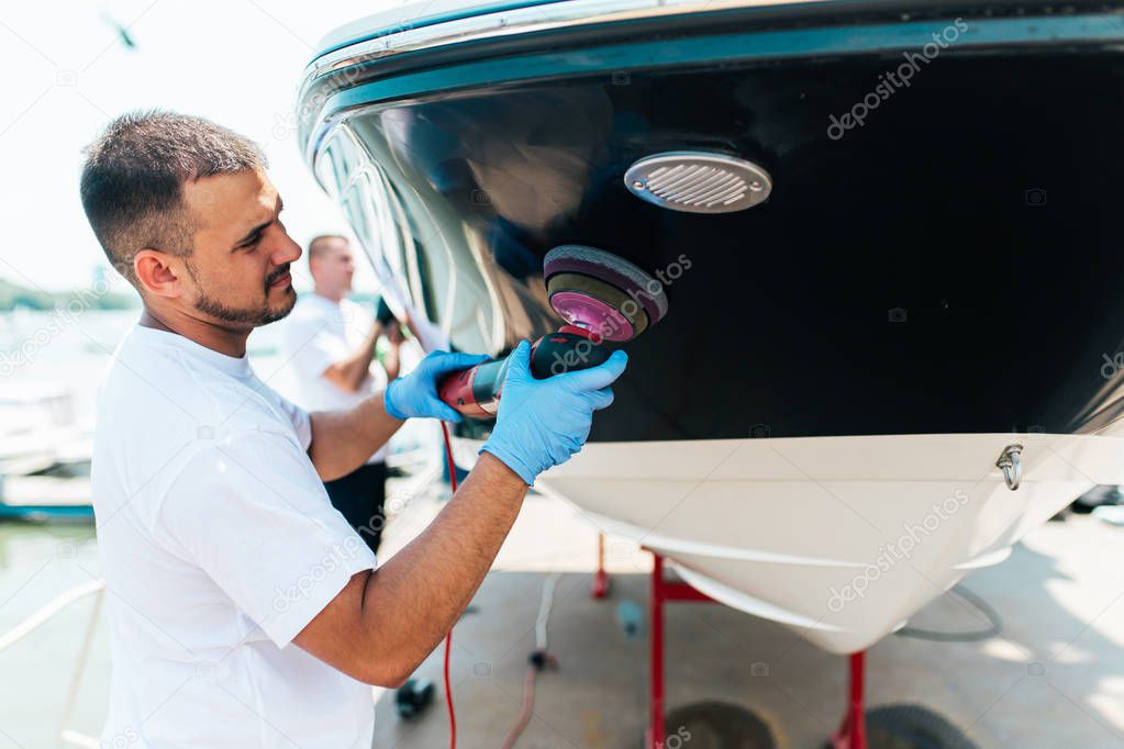 Boat maintenance - Man with orbital polisher polishing boat in marina. Selective focus.
