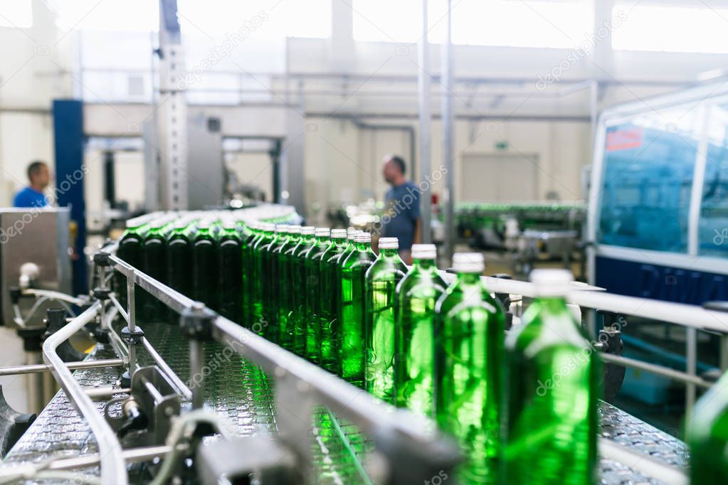 Water factory - Water bottling line for processing and bottling pure mineral water into green glass bottles. Selective focus.