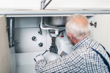 Üst düzey tesisatçı mutfakta tesisat aletleriyle çalışıyor. Yenileme.