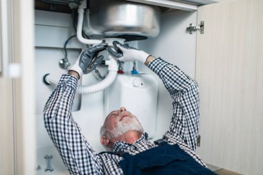 Üst düzey tesisatçı mutfakta tesisat aletleriyle çalışıyor. Yenileme.