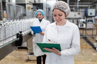 Şişeleme fabrikasındaki kadın işçiler sevkiyattan önce su şişelerini kontrol ediyorlar. Denetim kalite denetimi. 