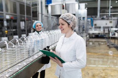 Şişeleme fabrikasındaki kadın işçiler sevkiyattan önce su şişelerini kontrol ediyorlar. Denetim kalite denetimi. 