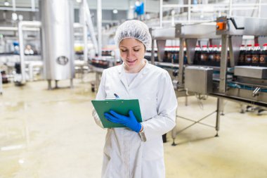 Şişeleme fabrikasında genç ve mutlu bir kadın işçi sevkiyattan önce meyve suyu şişelerini kontrol ediyor. Denetim kalite denetimi. 
