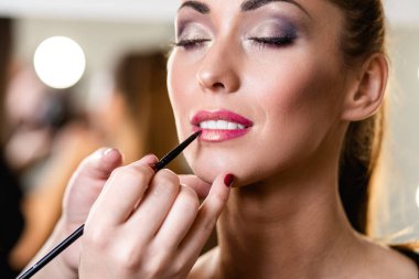 Makyaj sanatçısı, genç ve güzel bir bayana profesyonel makyaj yapıyor.