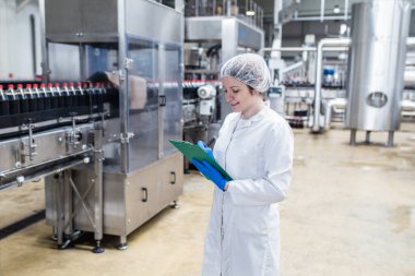 Şişeleme fabrikasında genç ve mutlu bir kadın işçi sevkiyattan önce meyve suyu şişelerini kontrol ediyor. Denetim kalite denetimi. 