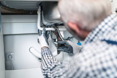 Üst düzey tesisatçı mutfakta tesisat aletleriyle çalışıyor. Yenileme.